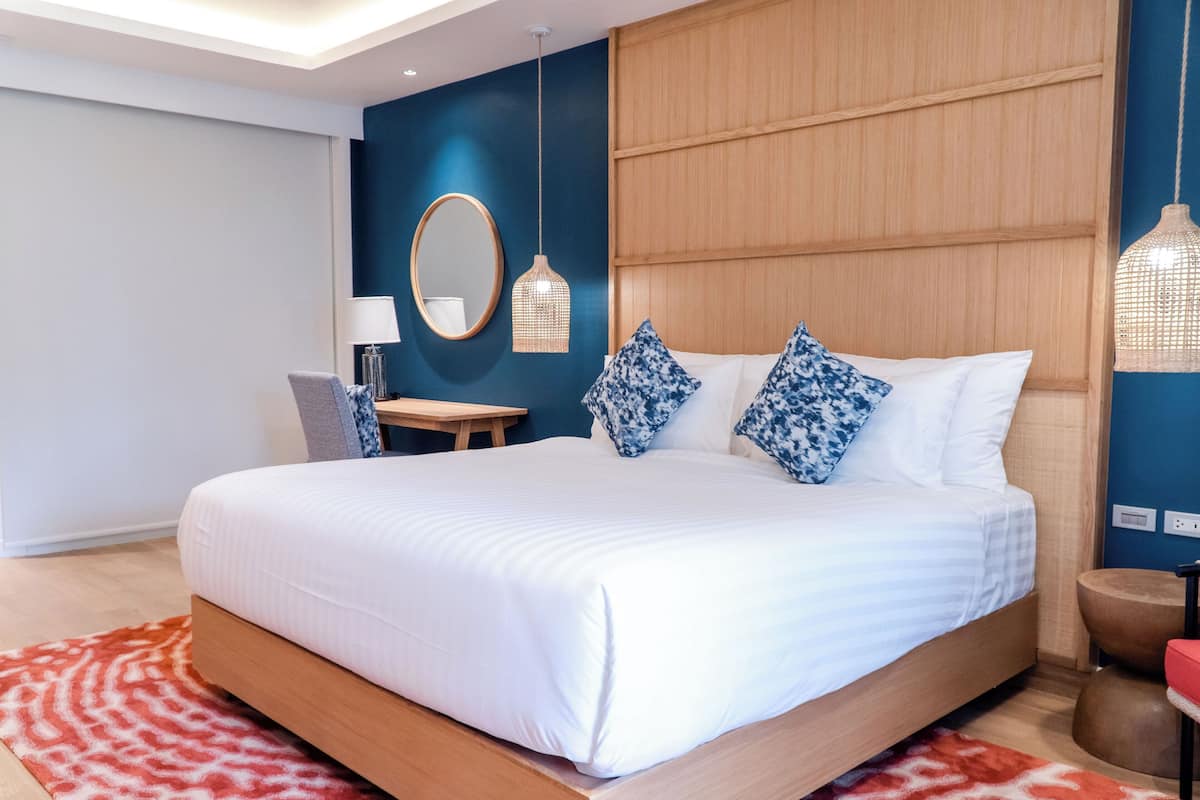 Ein modernes Hotelzimmer mit einem großen Bett, einem Holz-Kopfschild, einem kleinen Schreibtisch und einem Sessel.