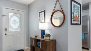 A modern entryway with a frosted glass door, a wooden console table with decorative items, a wall-mounted mirror, and a framed sign.