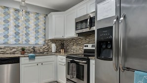 A modern kitchen with white cabinets, stainless steel appliances, a tiled backsplash, and a patterned curtain.