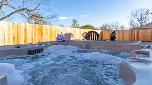 A hot tub with two towels, surrounded by a wooden fence and chairs.
