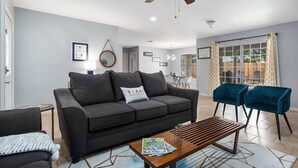 A modern living room with a dark grey sofa, a wooden coffee table, and teal armchairs.