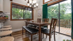 A dining area with a wooden table and chairs, a chandelier, and large windows with a view of trees. - So-Close Chalet - Easy walk to Bryce Resort! (Basye)