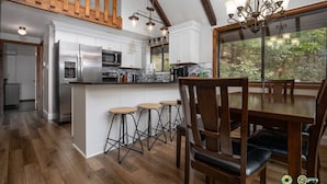 A modern kitchen with white cabinets, stainless steel appliances, and a wooden dining area with bar stools. - So-Close Chalet - Easy walk to Bryce Resort! (Basye)