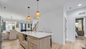Una cocina moderna con una isla central, iluminación colgante y una escalera que lleva a un nivel superior.