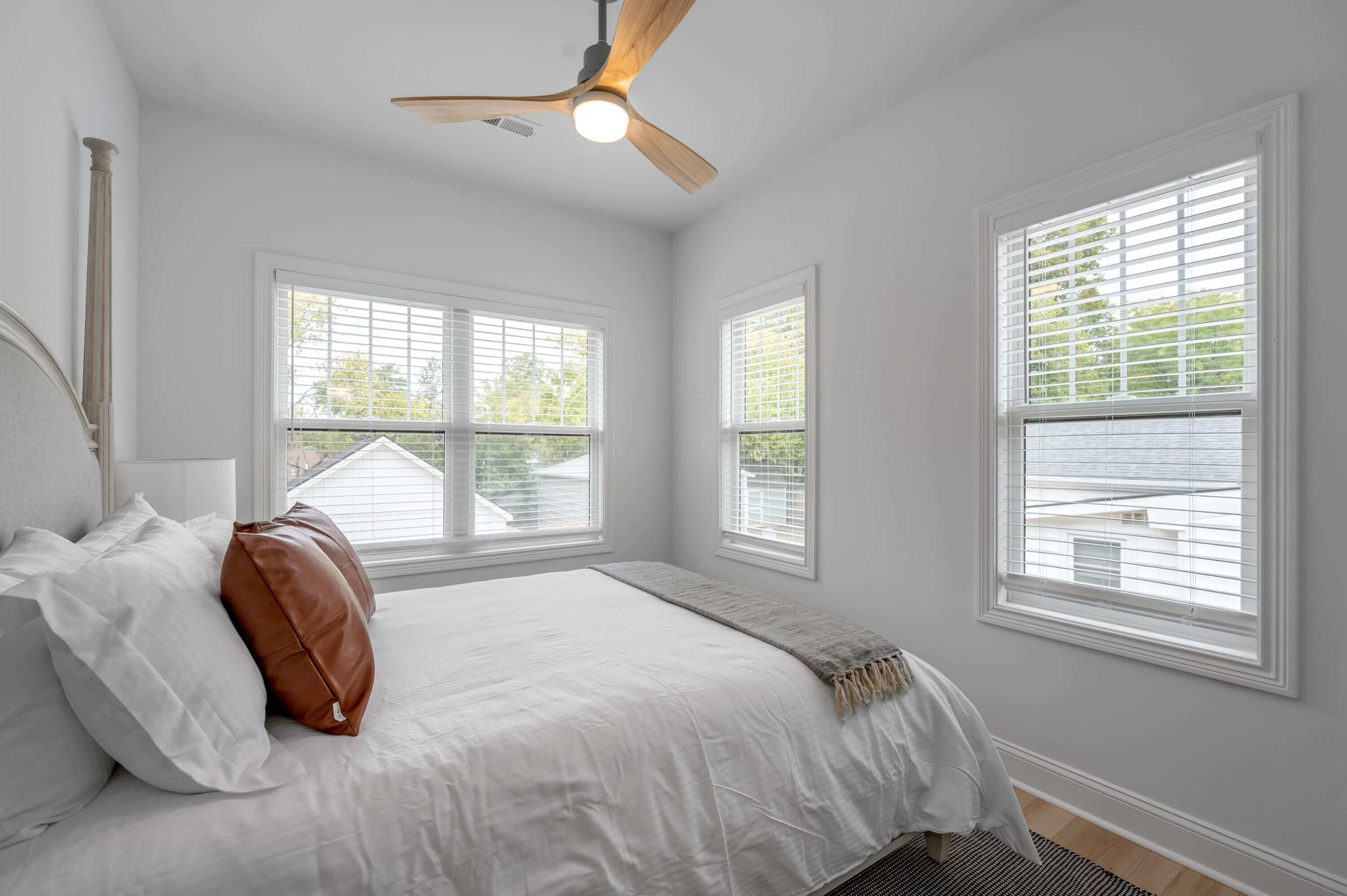 A bedroom with a bed, white walls, and windows with blinds.