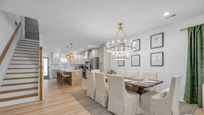 Una cocina moderna con armarios blancos, un comedor con mesa de madera y sillas blancas, y una escalera con peldaños de madera.