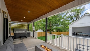Un patio exterior con un brasero, un sofá, una parrilla y una zona cubierta con una valla blanca.