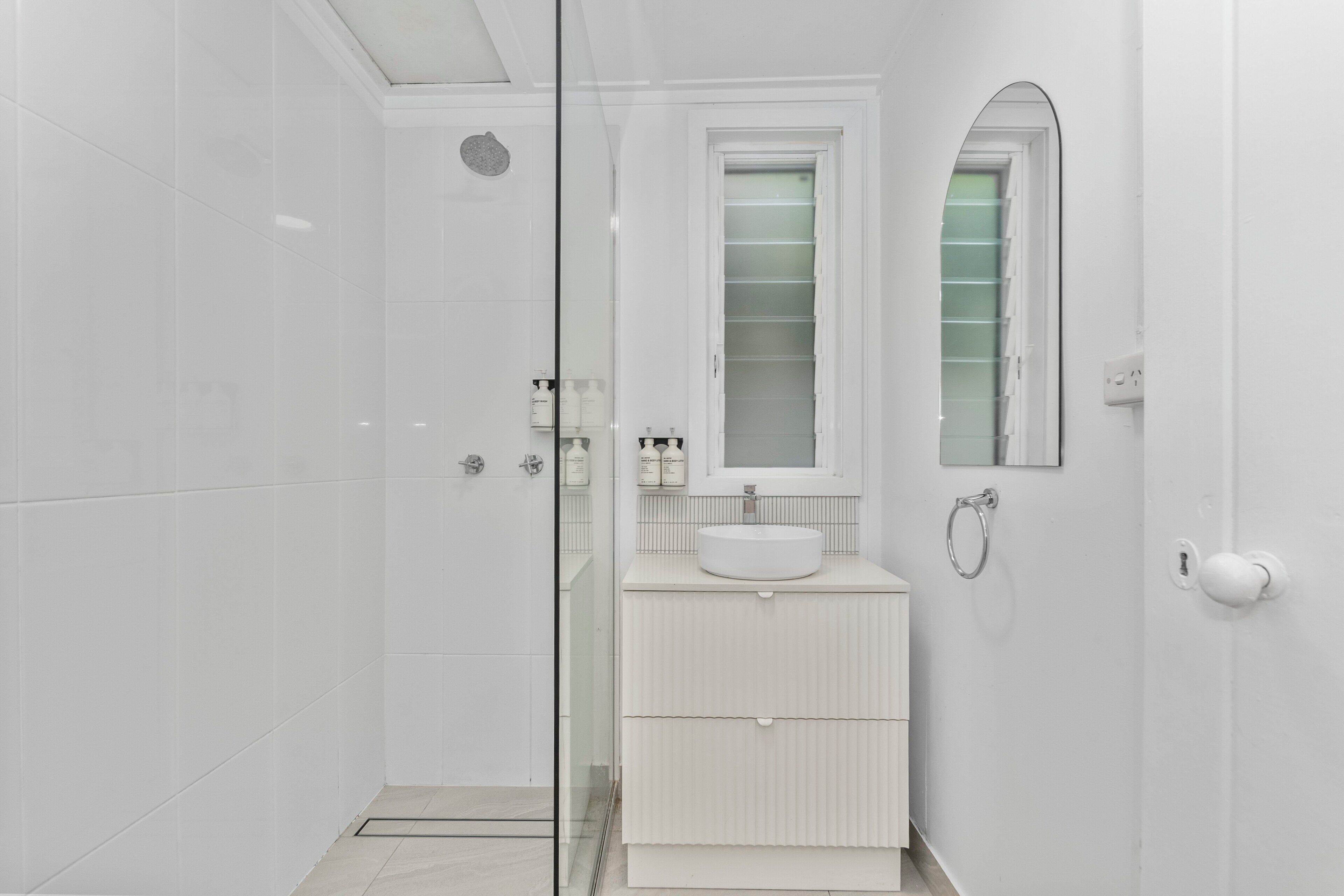 A modern bathroom with a glass shower enclosure, a white sink, and a mirror above it.