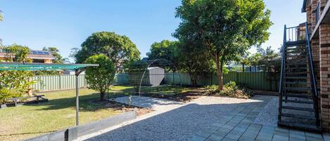 A backyard with a patio, a tree, a fence, and a building with a staircase.