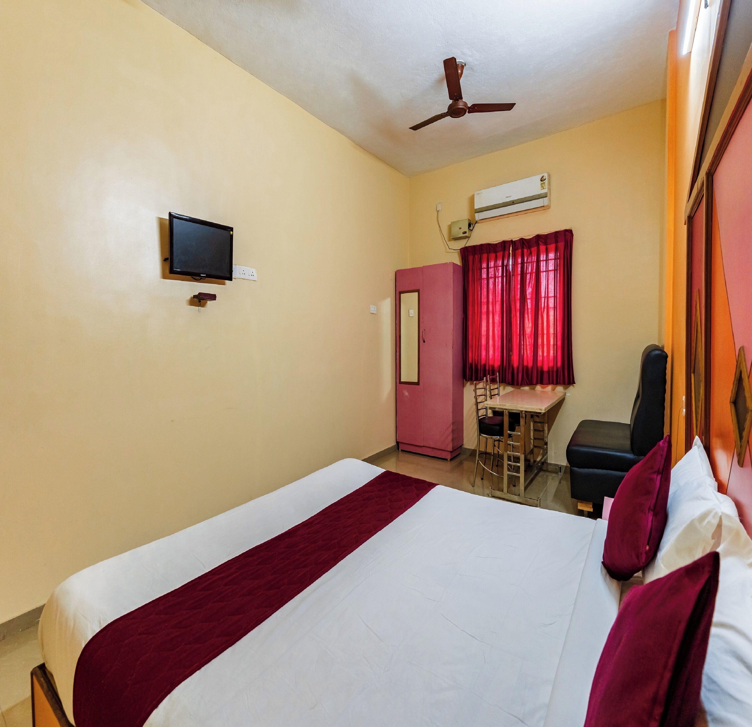 A hotel room with a bed, a desk, a chair, a wardrobe, and a ceiling fan.
