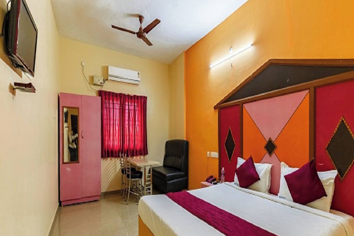 A hotel room with a large bed, a desk, a chair, and a ceiling fan.