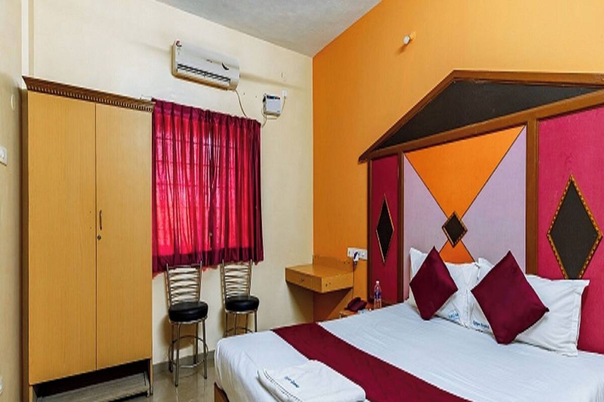 A hotel room with a bed, a wardrobe, two chairs, a desk, and an air conditioning unit.