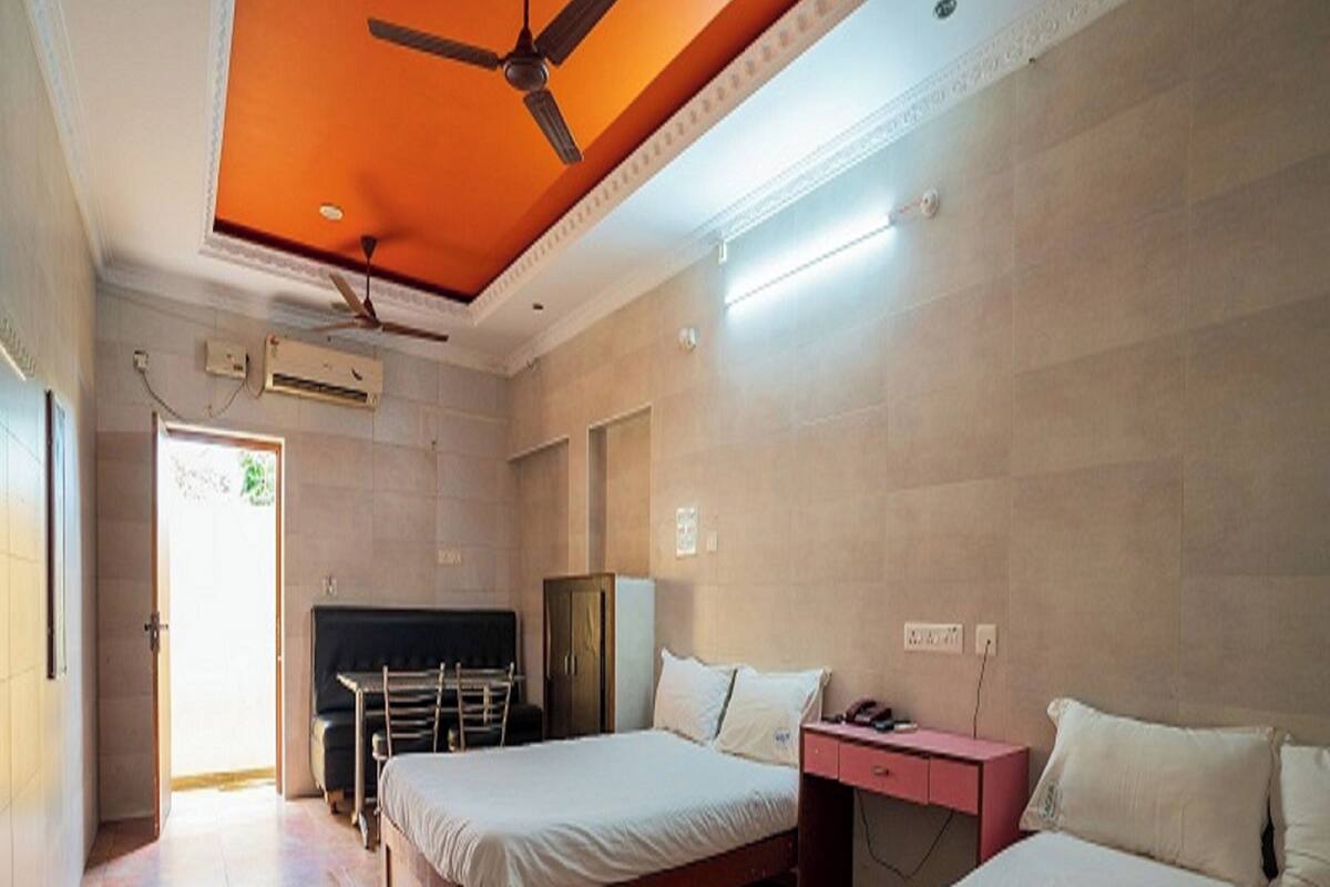 A hotel room with two beds, a desk, a chair, a TV, and a ceiling fan.