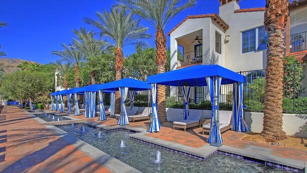 A pool area with blue umbrellas, lounge chairs, and palm trees. - Legacy Classic 2 bedroom condo (La Quinta)