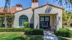 A stucco house with a tiled roof, a large arched window, and a front porch with a table and chairs. - Legacy Classic 2 bedroom condo (La Quinta)