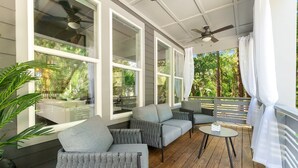 A covered outdoor seating area with gray upholstered chairs, a round table, and large windows offering a view of a garden and a building. - Secret Pool Cabana- Mins to Downtown and Beach (St. Augustine)