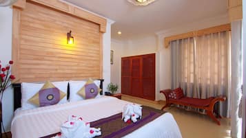 Habitación de hotel con una cama grande, cabecera de madera, un banco de madera y un ventanal con cortinas.