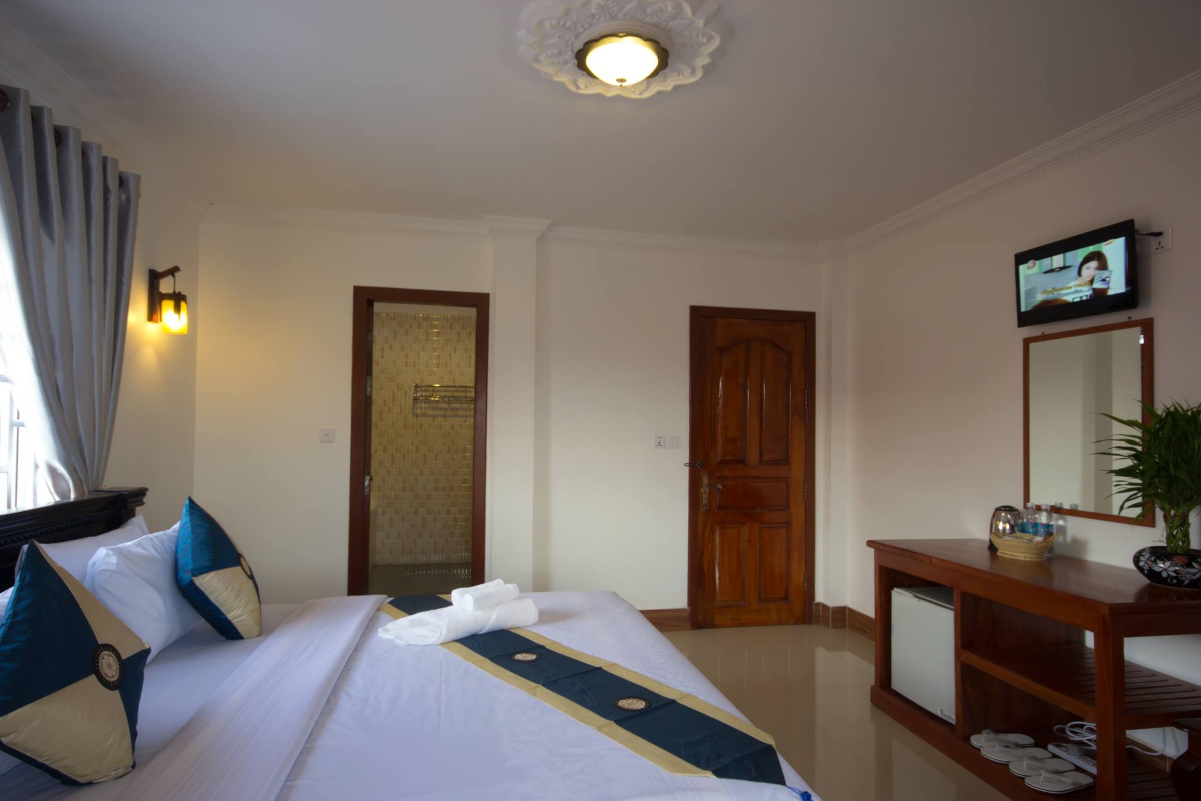 A hotel room with a bed, a wooden desk, a television, and a mirror.