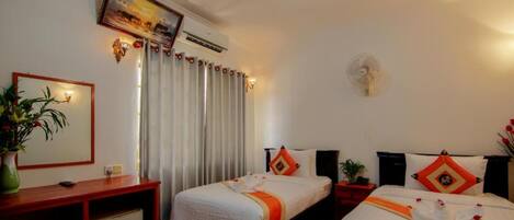 A hotel room with two beds, a desk, a chair, a small table, a plant, a wall-mounted air conditioner, and a ceiling fan.