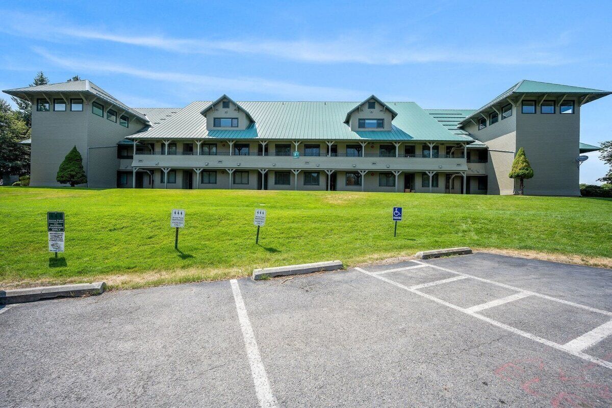 A large, multi-story building with a symmetrical facade, a central entrance, and a parking area in the foreground.