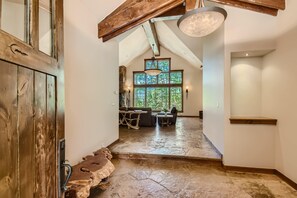 Un interior rústico con suelo de piedra, vigas de madera y un comedor con vistas a árboles.