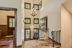 Una escalera con barandilla de hierro forjado, un candelabro y varias ventanas con marcos de madera.