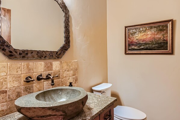 Un baño con un lavamanos de piedra, un espejo con marco de madera, un inodoro y un cuadro en la pared.