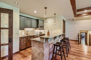 Una cocina con encimeras de granito, una isla central con taburetes y vigas de madera en el techo.