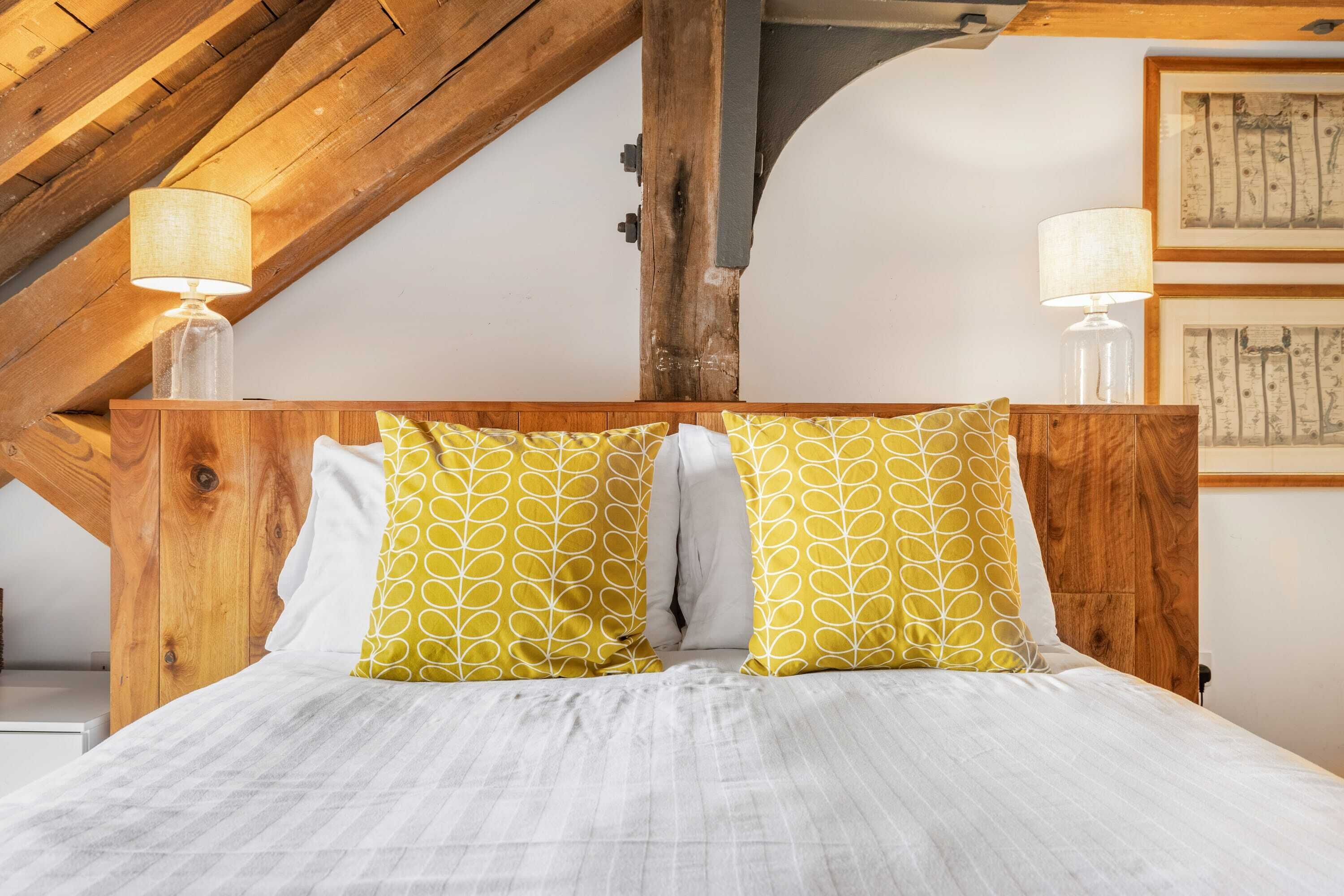 A bed with a wooden headboard, two pillows with a leaf pattern, and two bedside lamps.
