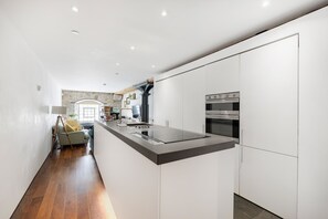 Una cucina moderna con mobili bianchi, un'isola centrale dotata di piano cottura integrato e una parete decorativa in pietra.