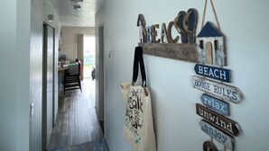 A hallway with a welcome sign, a beach-themed wall decoration, and a bag hanging on the wall. - Bugsy's By the Beach ~ Hot Tub, Hammock Station & A/C (Long Beach)