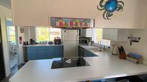 A modern kitchen with a central island, blue cabinets, and a decorative crab wall art piece. - Bugsy's By the Beach ~ Hot Tub, Hammock Station & A/C (Long Beach)