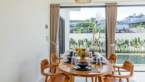 A dining area with a table set for six, large windows, and a view of a pool and greenery.