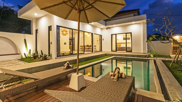 A modern outdoor pool area with lounge chairs and an umbrella, surrounded by a well-maintained garden and a house with large windows.