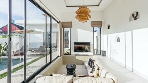 A modern living room with a large TV, comfortable seating, and a view of a pool and outdoor area.