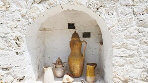 A white stone wall with a small arched niche containing several pottery items. - Trullo Agapanthus (Ostuni)