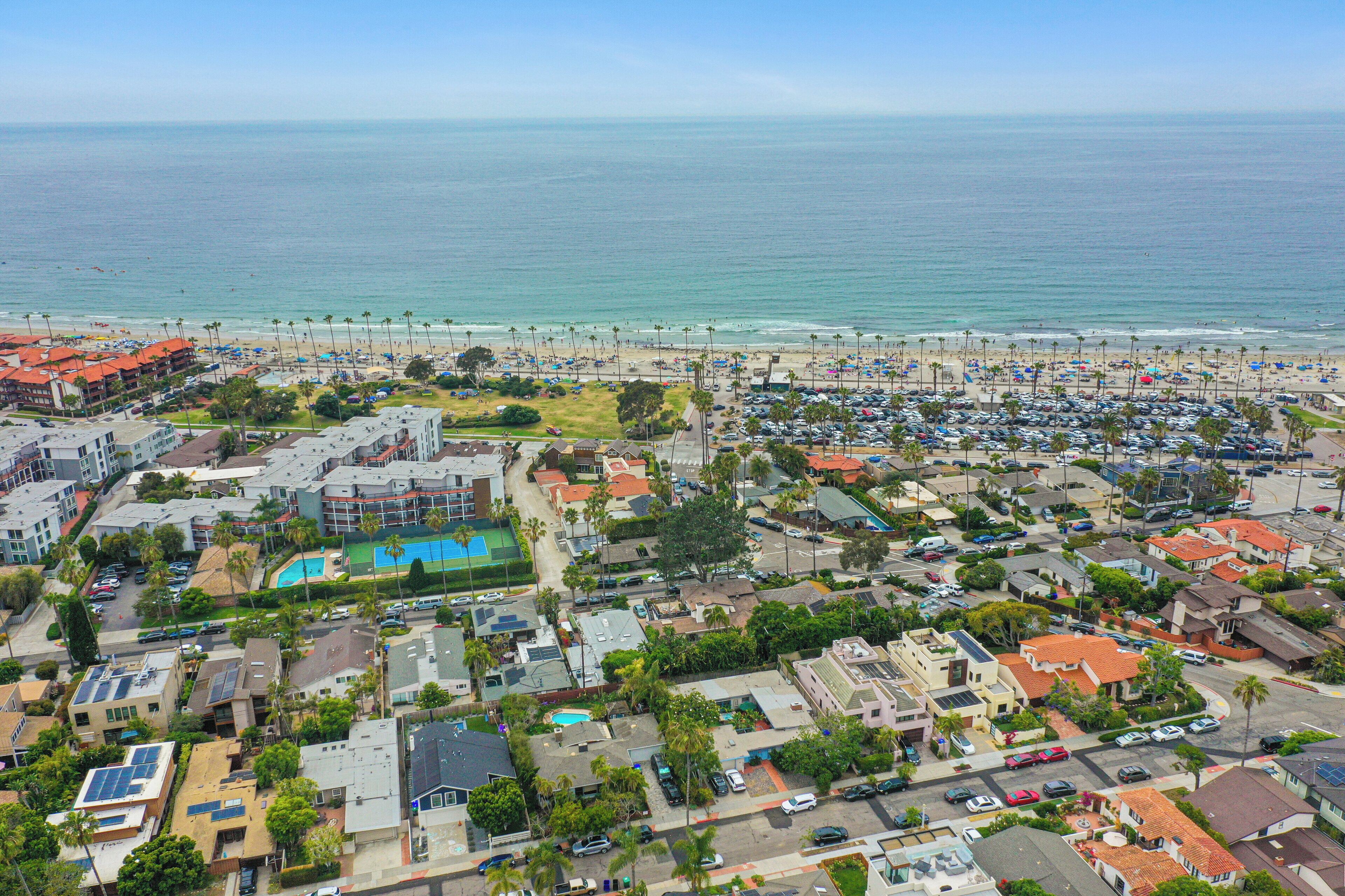 Vista aérea de un pueblo costero con playa, estacionamientos y edificios residenciales.