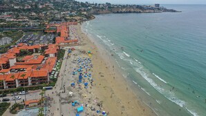 Un hotel costiero con diversi edifici, una spiaggia con ombrelloni e vista sull'oceano.