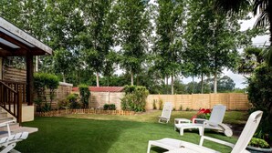 Un jardin avec une pelouse artificielle, des chaises longues blanches et une clôture en bois.