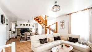 Un salon spacieux avec un grand canapé en forme de L, une table basse en bois et un escalier menant à l’étage supérieur.