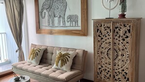 Una sala de estar con un sofá color beige, una obra de arte con un elefante enmarcado, un mueble decorativo y una pequeña mesa redonda con una tetera.