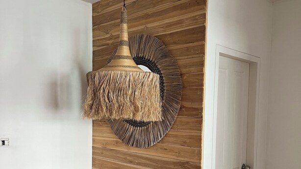 Una habitación con pared de madera, una lámpara de fibra trenzada, dos sillas de madera y una puerta blanca.