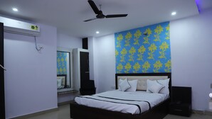 A bedroom with a bed, a ceiling fan, an air conditioner, a mirror, and a wall with a floral pattern. - Hotel Axiom Prime (Lucknow)