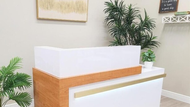 A reception desk with a white top and wooden base, flanked by potted plants. - Hotel Axiom Prime (Lucknow)