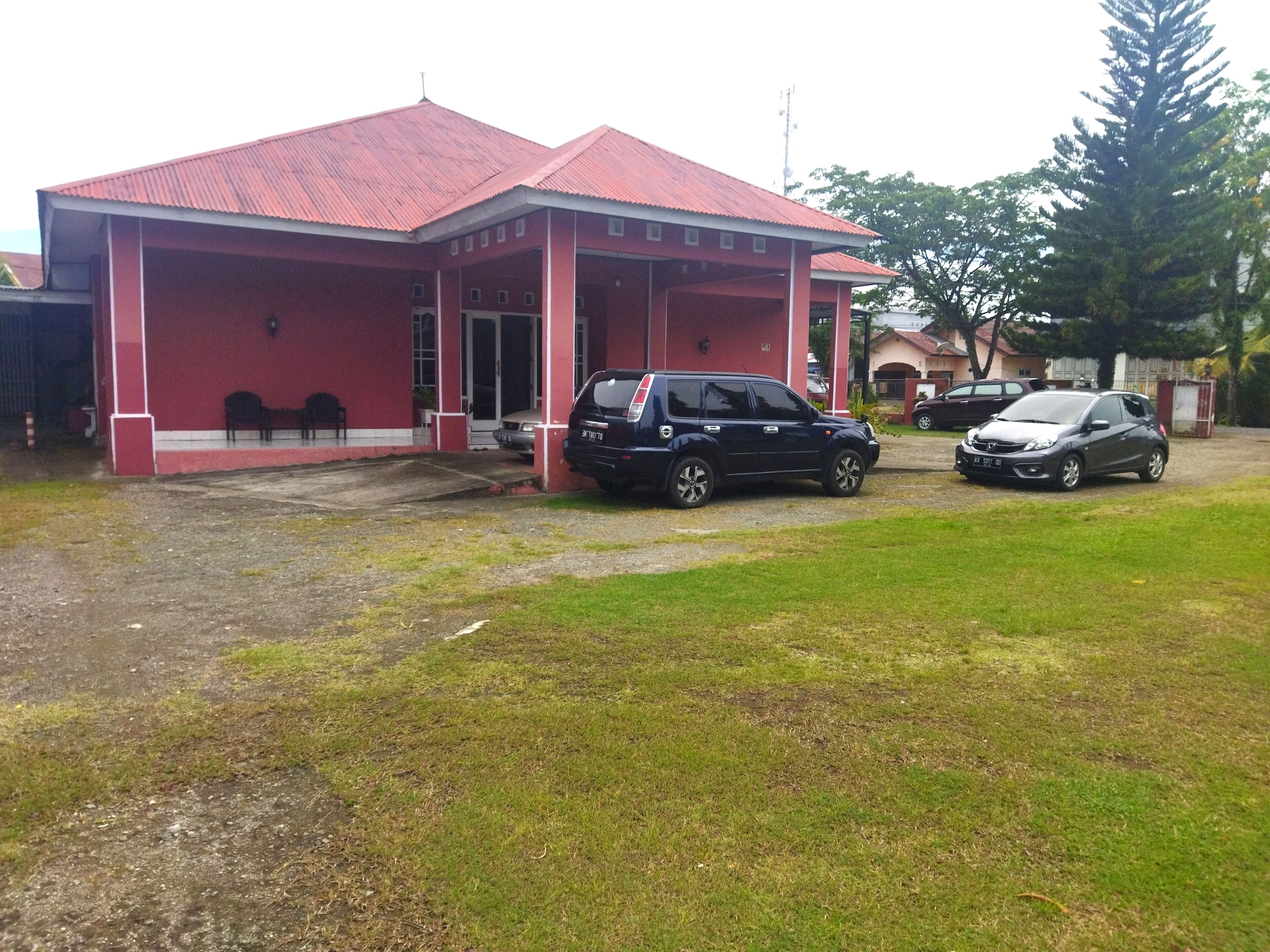 Um edifício com telhado vermelho e varanda coberta. Dois carros estacionados em frente.