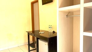 A small room with a desk, a chair, a refrigerator, a water bottle, and a remote control. - Hotel O Wisma Phinisi Syariah Near Mall of Pinrang Sejahtera (Pinrang)