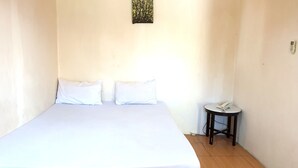 A single bed with white bedding, a small bedside table with a telephone, and a wall-mounted light fixture. - Hotel O Wisma Phinisi Syariah Near Mall of Pinrang Sejahtera (Pinrang)