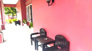 A covered outdoor seating area with a red wall, black chairs, and a wall-mounted lamp. - Hotel O Wisma Phinisi Syariah Near Mall of Pinrang Sejahtera (Pinrang)