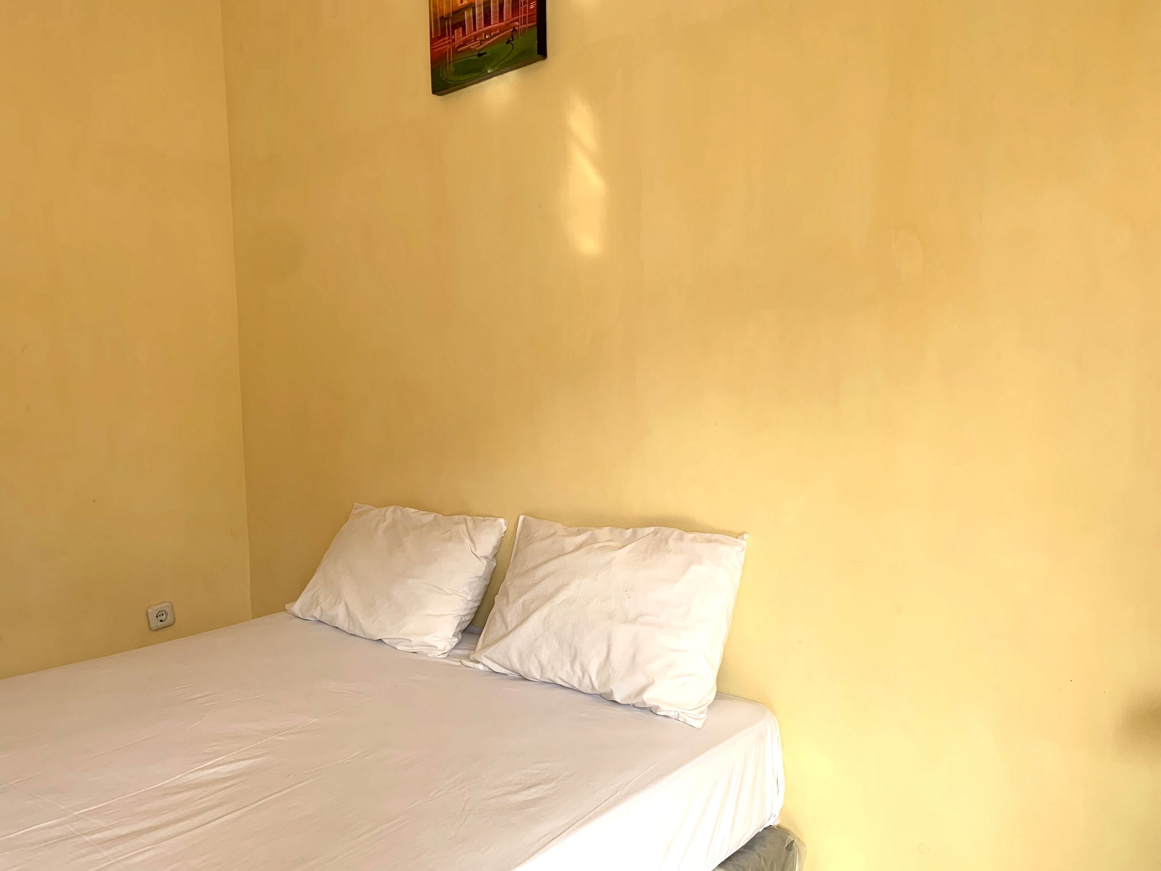 A single bed with white bedding in a room with yellow walls.