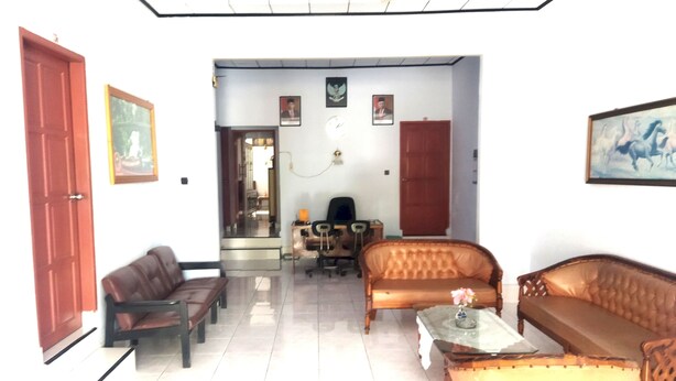 A living room with a brown sofa, a wooden coffee table, and a red door. - Hotel O Wisma Phinisi Syariah Near Mall of Pinrang Sejahtera (Pinrang)